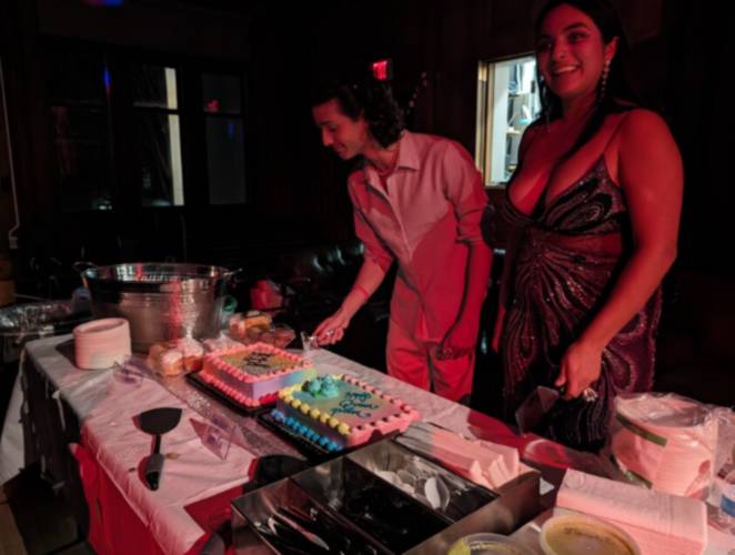 Felipe Mendonca (left) and Rosario Rosales get ready to cut a vanilla and a chocolate cake as a crowd of attendees gather around them. Both cakes are decorated with the words 
